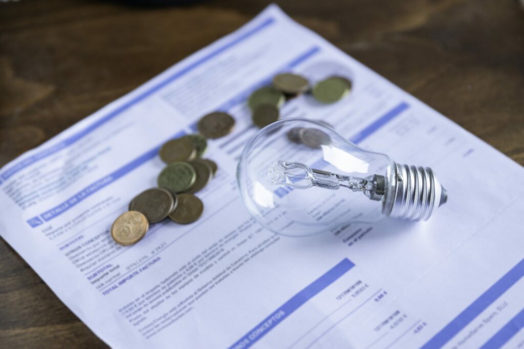 Paper bill with coins and a lightbulb on top of it.