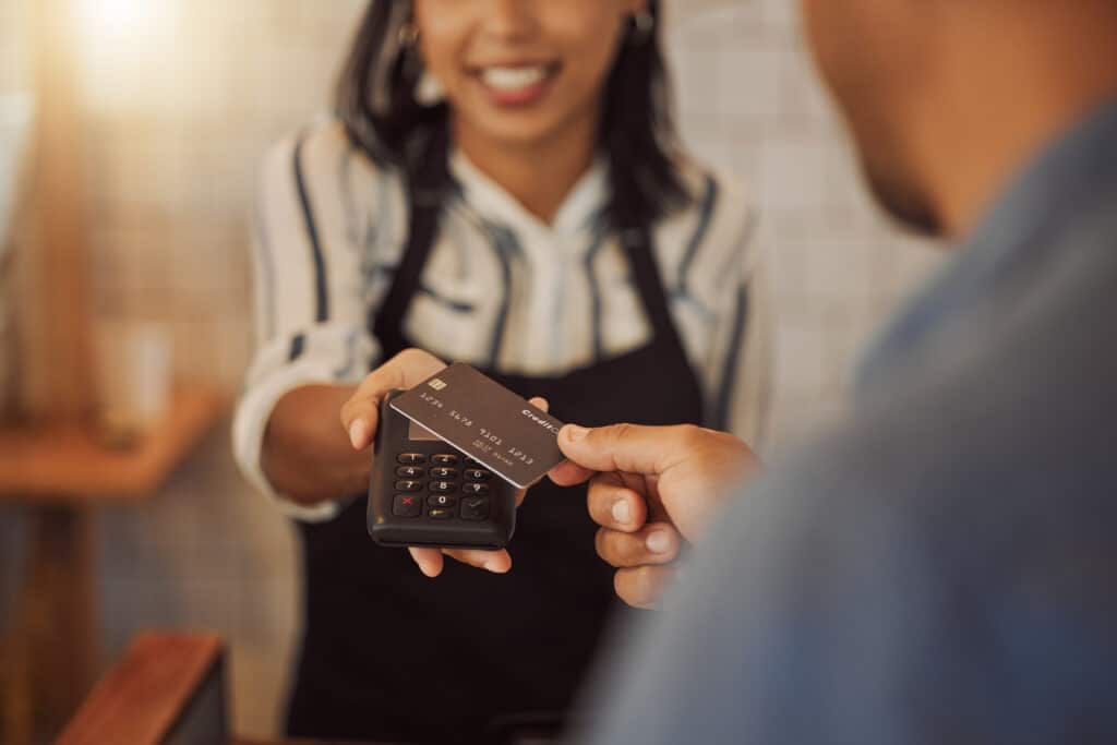 Customer using a credit card to tap for payment. Barista helping a customer making online payment. Customer using debit card to make NFC machine payment. A customer paying their bill in a coffeeshop