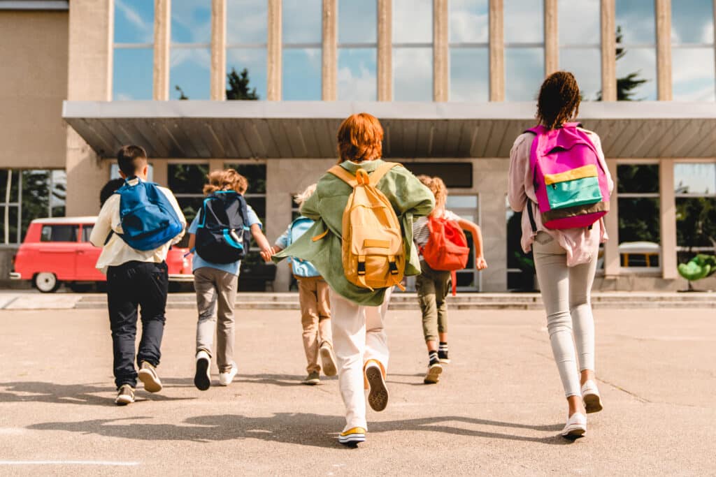 Kids walking into school with bright backpacks on. Topic: back to school shopping.