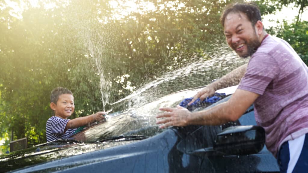 car wash at home. Boy helping dad washing car on water splashing with sunlight at home, Slow Motion. Activity holidays in family.