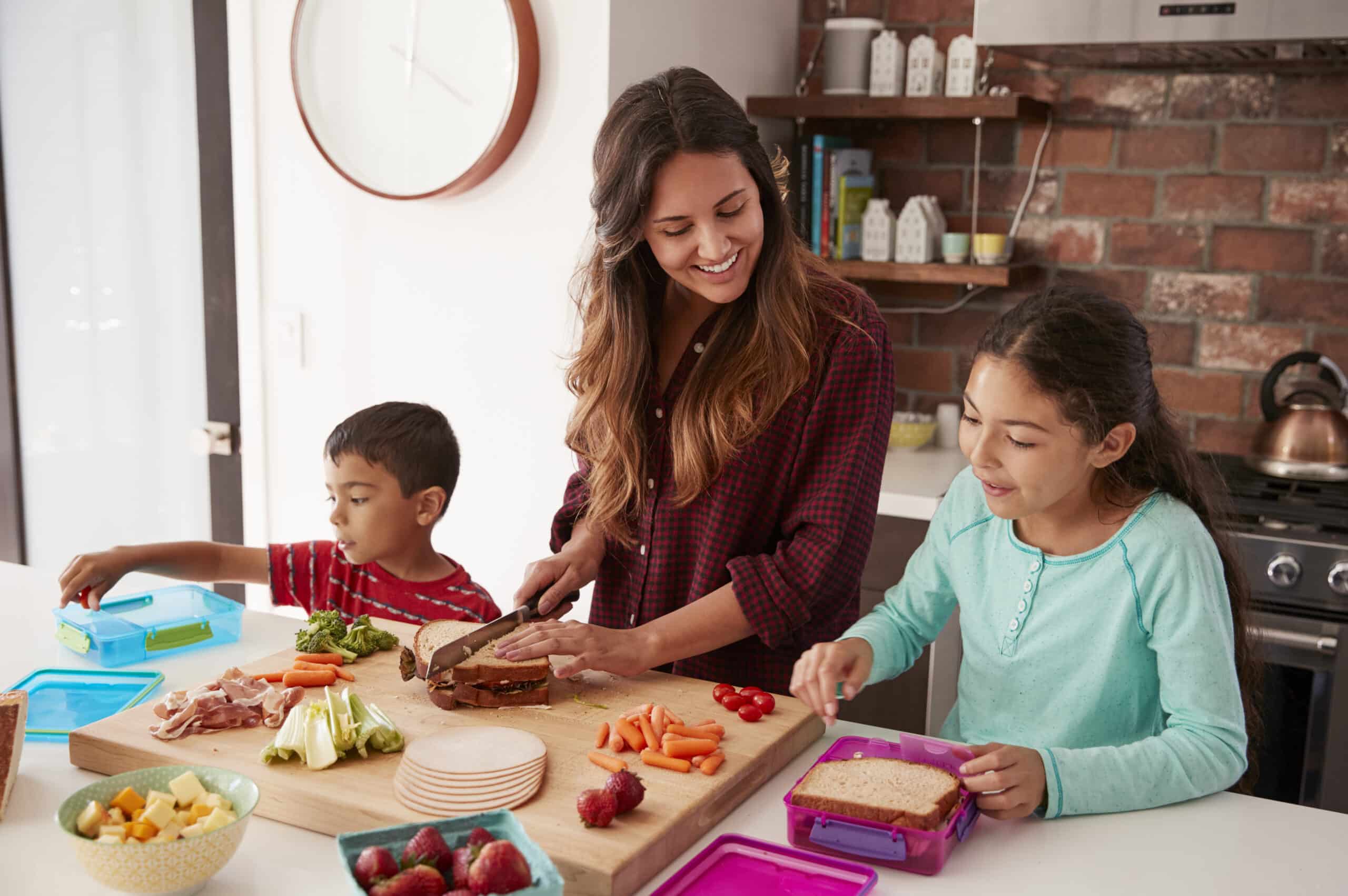 Two kids helping their mom make food with fresh fruits and veggies