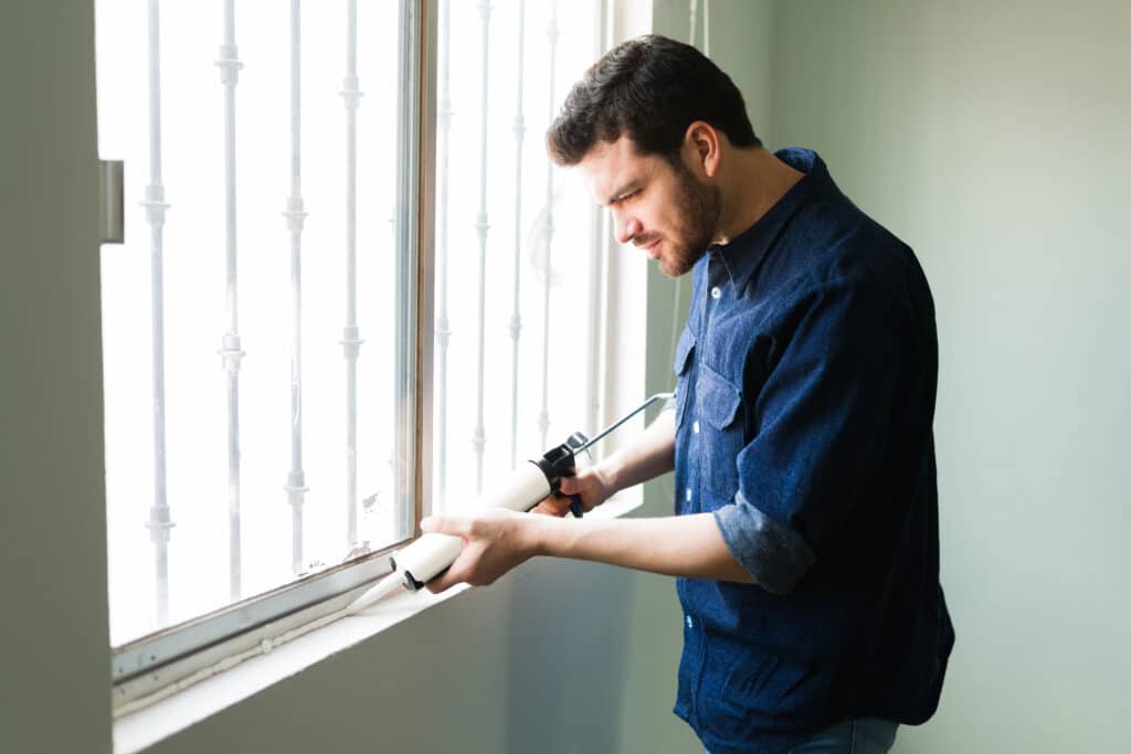 DIY home projects. Attractive young man and handyman insulating his home windows during the winter season