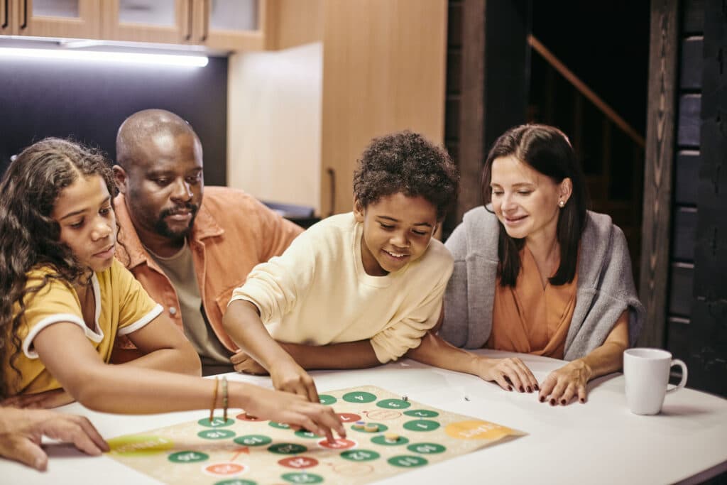 Rainy day activities. Happy parents sitting at the table and playing with children in board game at home.