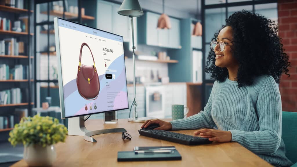 Latina Female Using Desktop Computer with Clothing Online Web Store to Choose and Buy Clothes from New Collection. Female Browsing the Internet at Home Living Room while Sitting at a Table