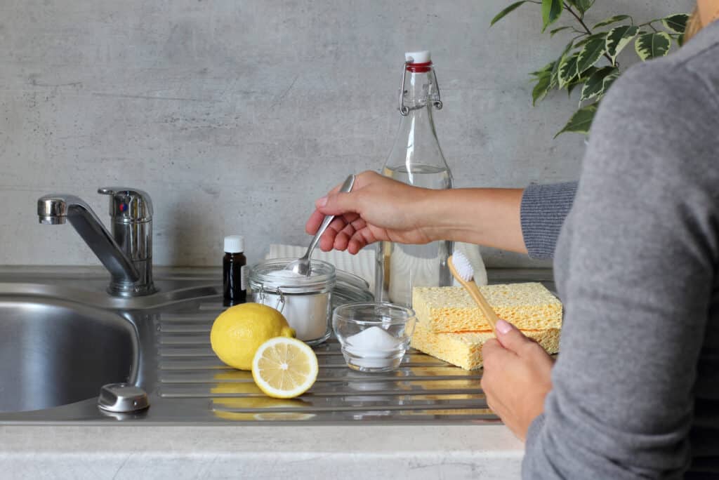 baking soda uses. Vinegar, bicarbonate of soda, lemon, sponge, bamboo toothbrush, cotton towels on the kitchen stainless stil sink next to the tap.