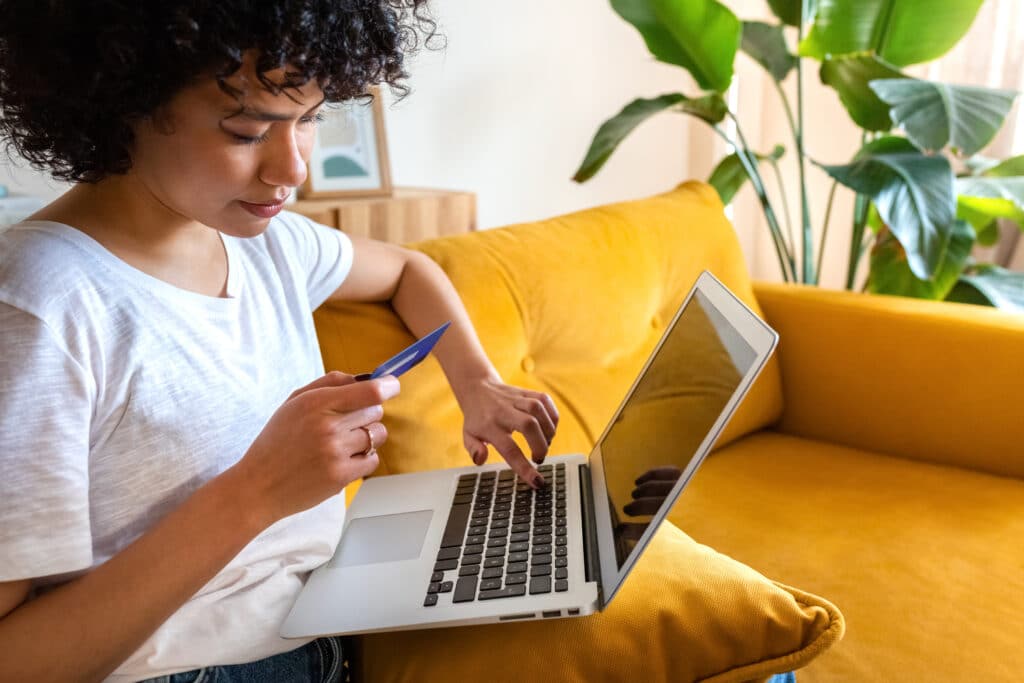 credit card limit increase cons. Close up of african american woman sitting on the couch using credit card and laptop to shop online from home. Copy space. E-commerce concept.