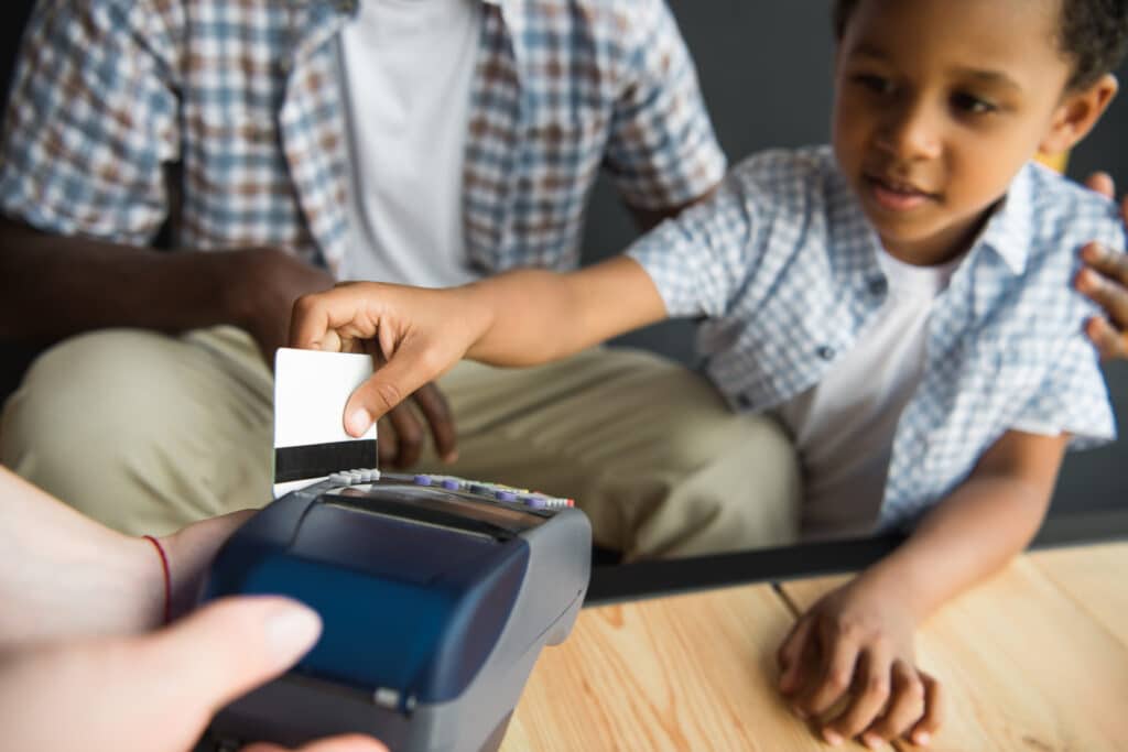 cropped shot of father and son using credit card while paying bill in cafe with debit card for kids.