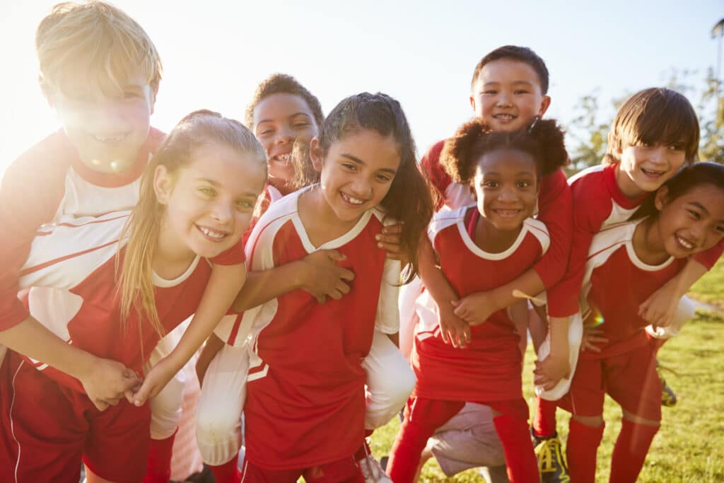 how to budget for kids' sports. Kids in elementary school sports team piggybacking outdoors