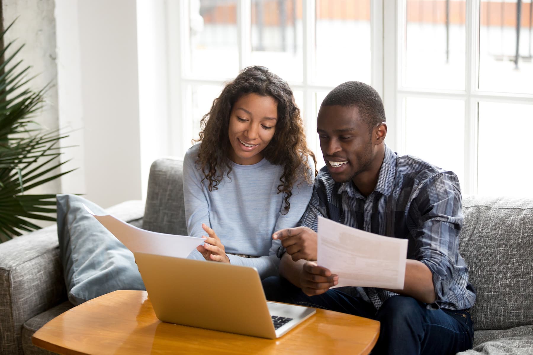 short-term savings goals. African black married couple sitting on sofa at home read documents paper checking bills, bank account balance feeling satisfied and happy. Refund income last loan payment good news concept