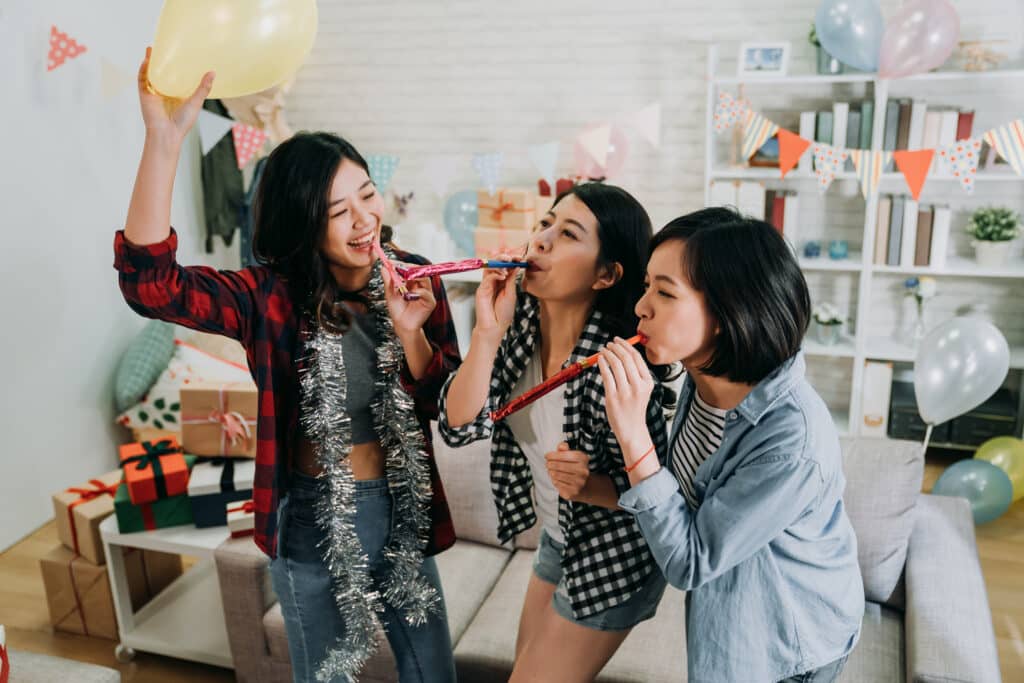 Special occasion, young girls best friends celebrating graduation party in house. female students playing with whistles and balloons having fun at decorated home. enjoyment friendship never end concept.