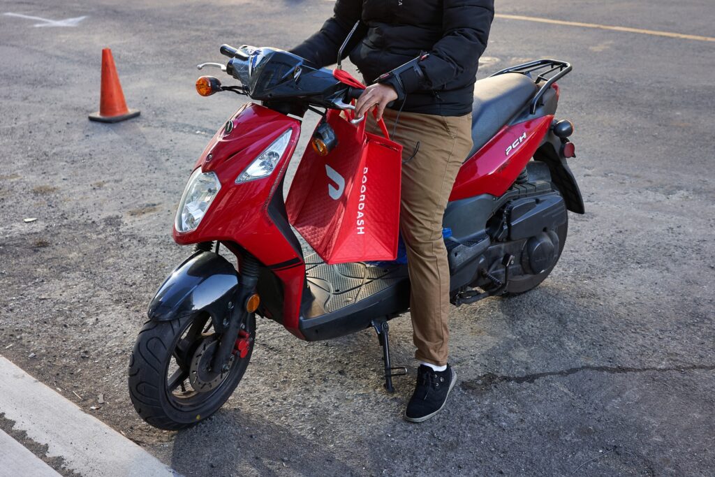 DoorDash driver on red moped with bag.