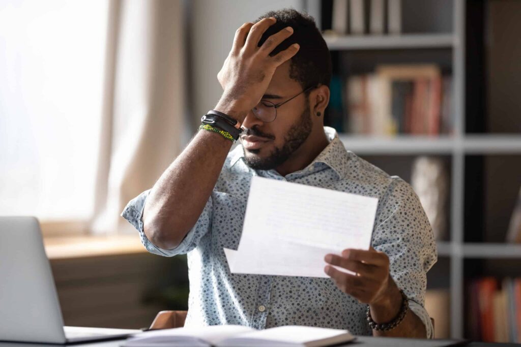 budgeting mistakes: African businessman holding letter reading bad bank news about debt