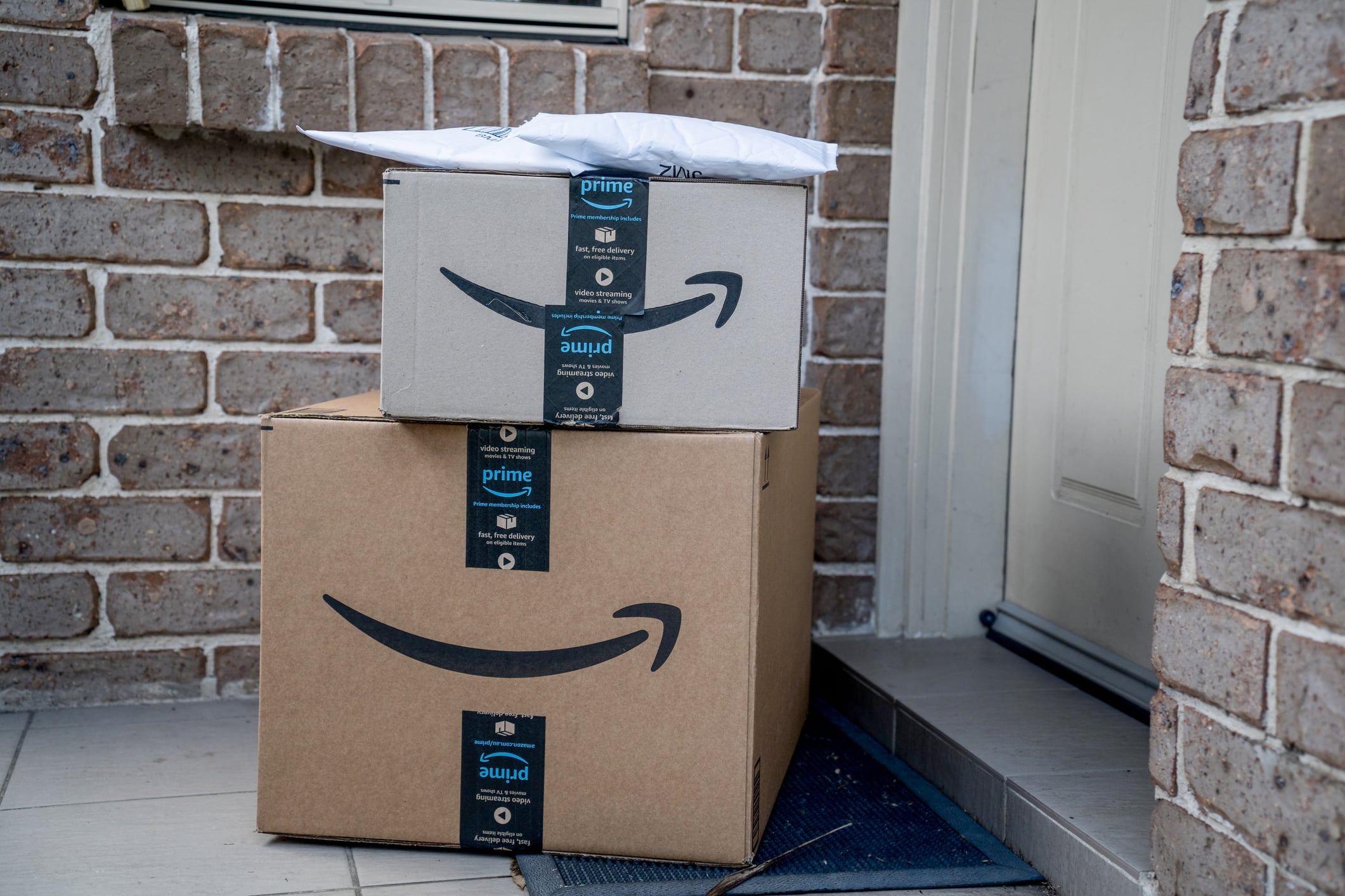 Prime Day Amazon boxes and envelope on a porch with brick wall behind them.