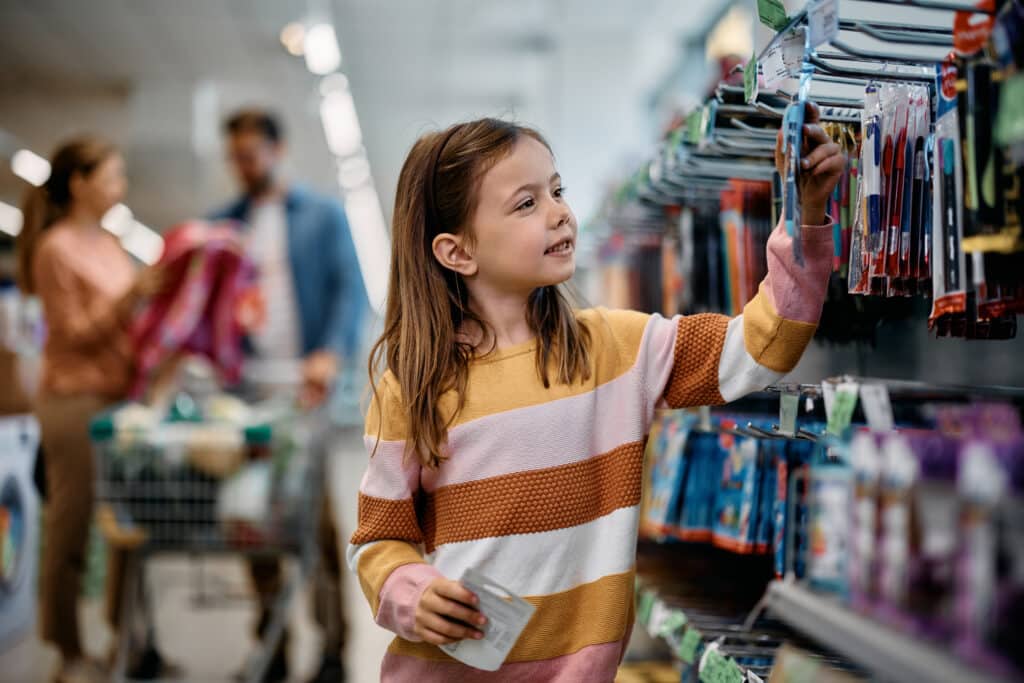 back to school shopping. Smiling little girl buying school supplies while being with her parents in a bookstore.