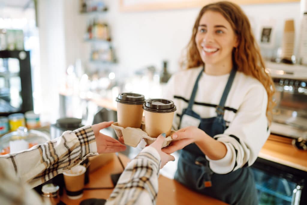 Everyday things. Smiling barista- girl giving take away coffee cups to a customers.