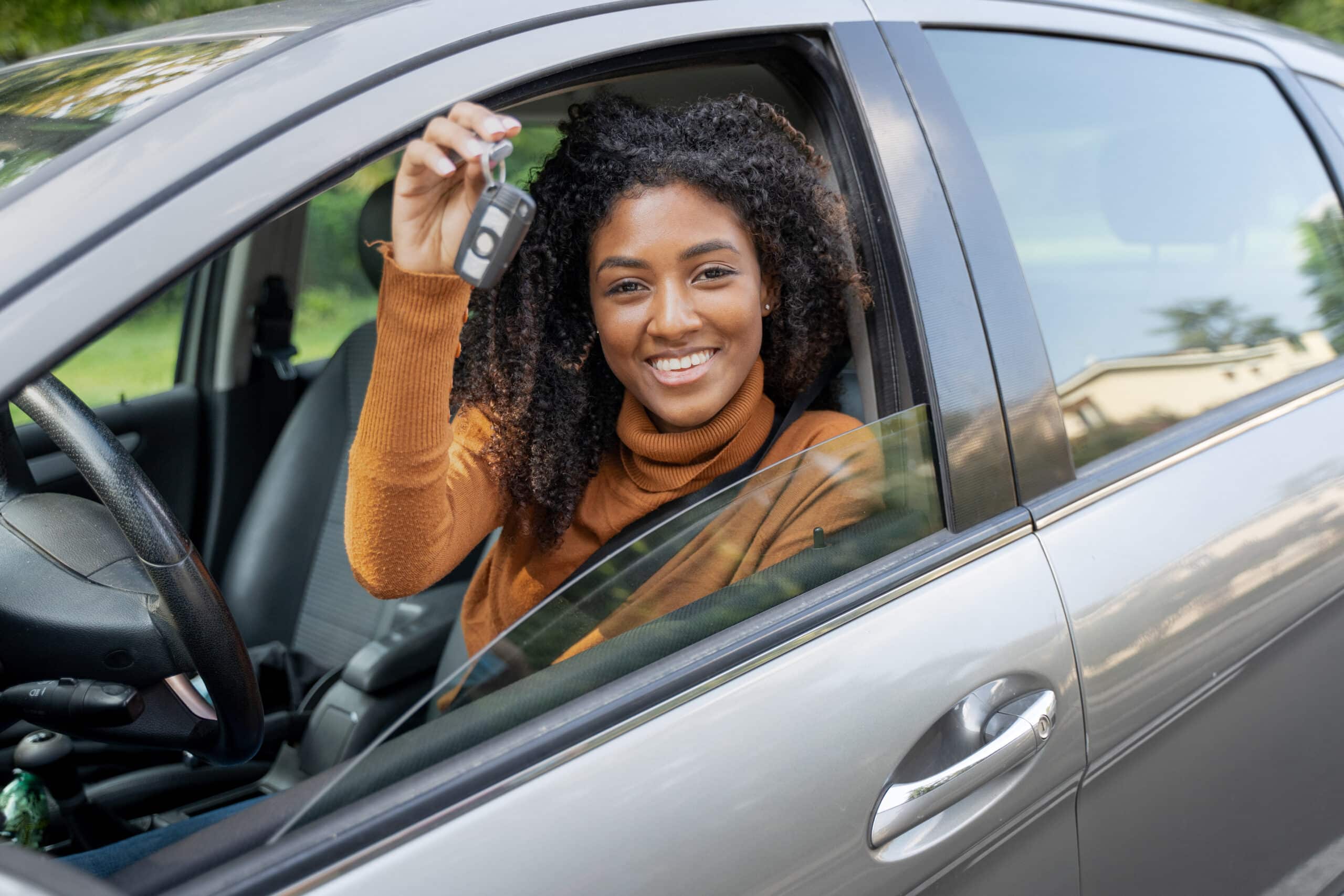 Get the best price on a car: New car owner. happy black woman sitting in a grey car, showing car key.