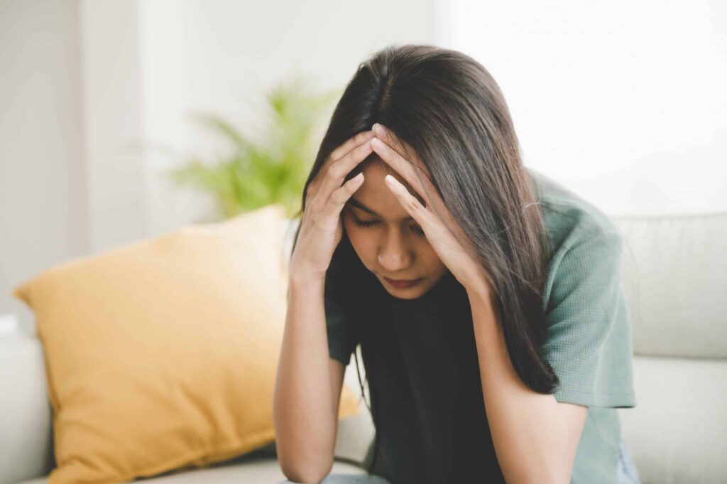 Upset asian woman frustrated by debt, sitting on couch, feeling despair and anxiety, loneliness, having psychological trouble