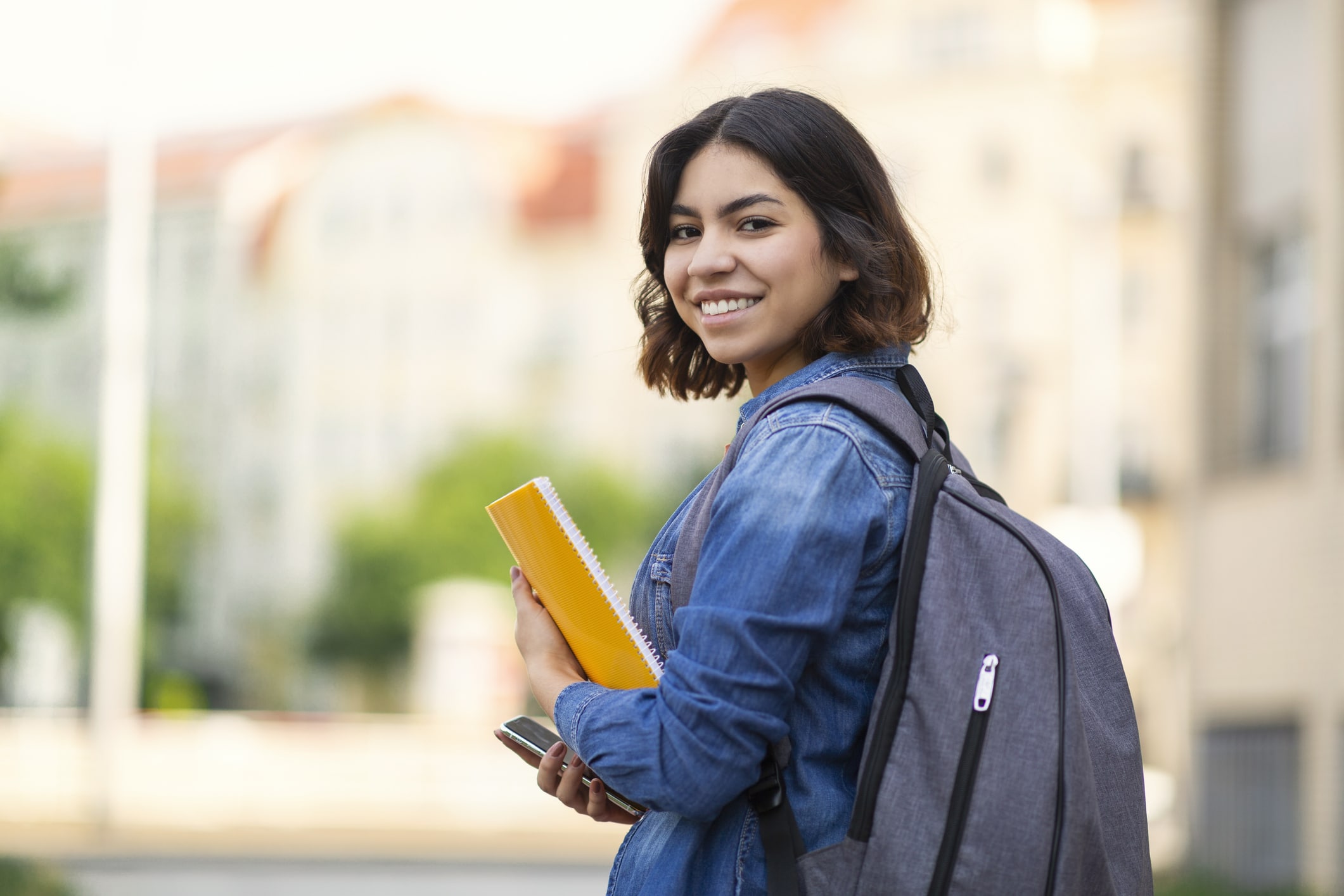 Student loan. Smiling Young Arab Female Student With Workbooks And Backpack Standing Outdoors, Happy Middle Eastern Millennial Woman Posing Outside At University Campus, Turning At Camera, Copy Space.