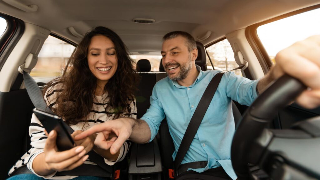 Road trip on a budget. happy couple driving and looking at a phone screen.