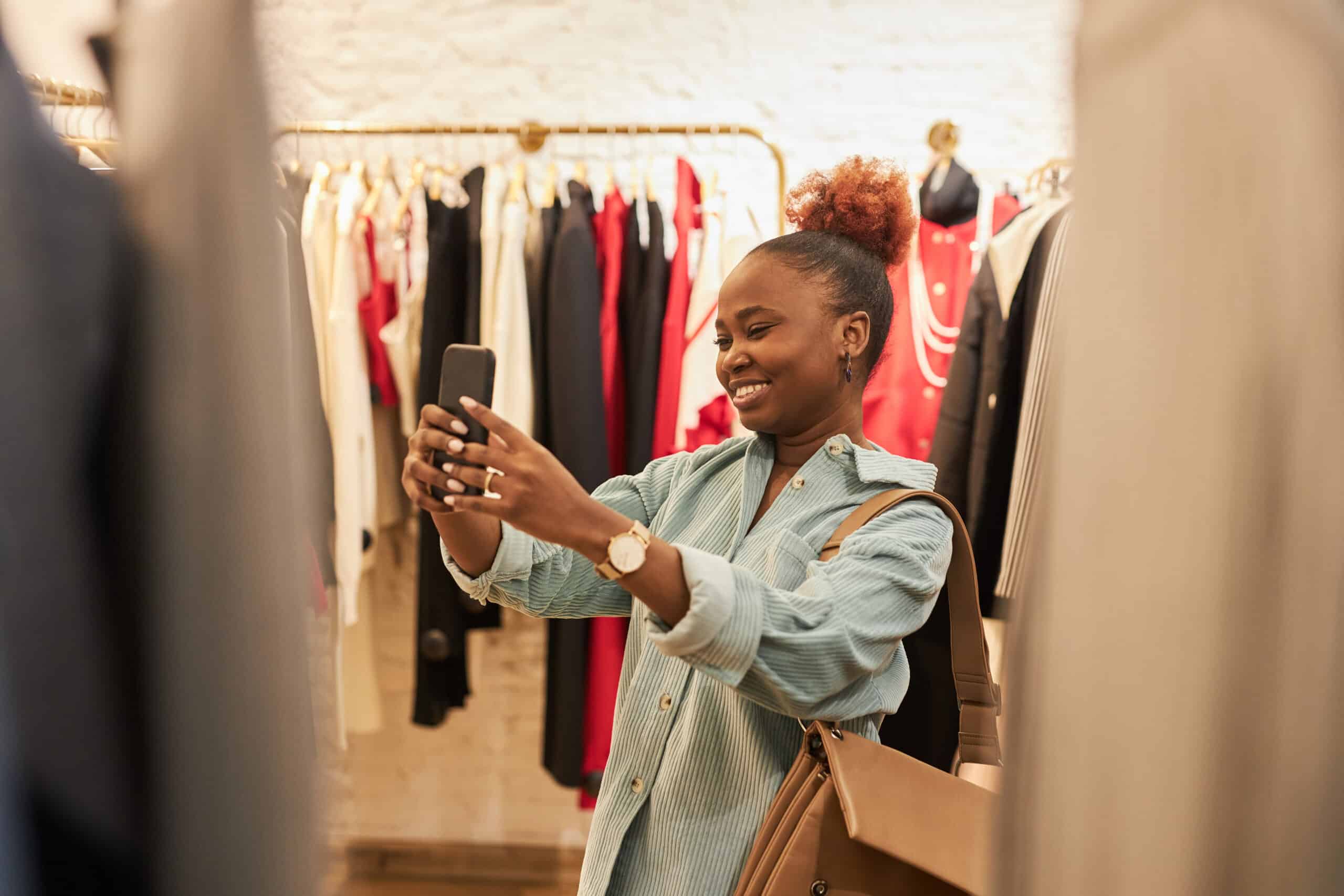 thrifting. Waist up portrait of smiling black woman taking selfie photos in clothing store and enjoying shopping