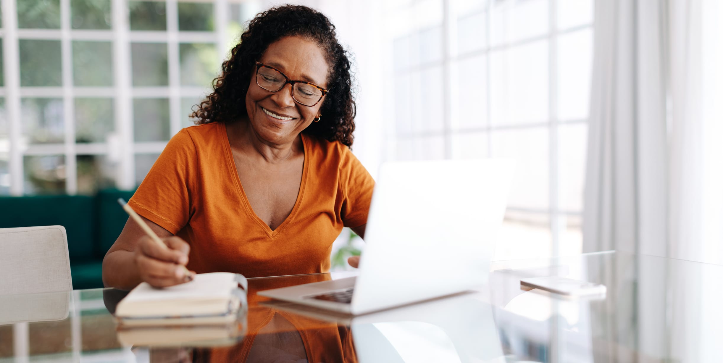 Types of budgets. Happy senior woman sitting at a table in her home office, drafting her last will and testament in a journal and taking care to allocate her assets. Retired woman leaving a plan in place for the future.