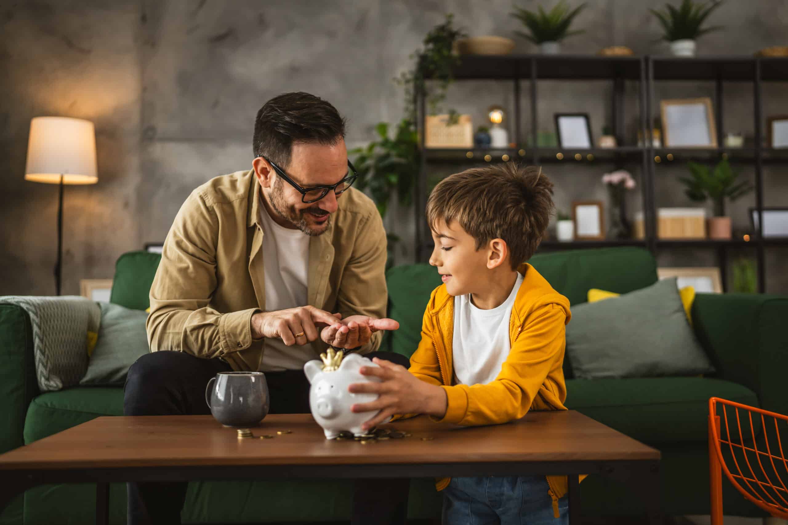Talk money with your kids. Father show son how to save money at piggy bank at home
