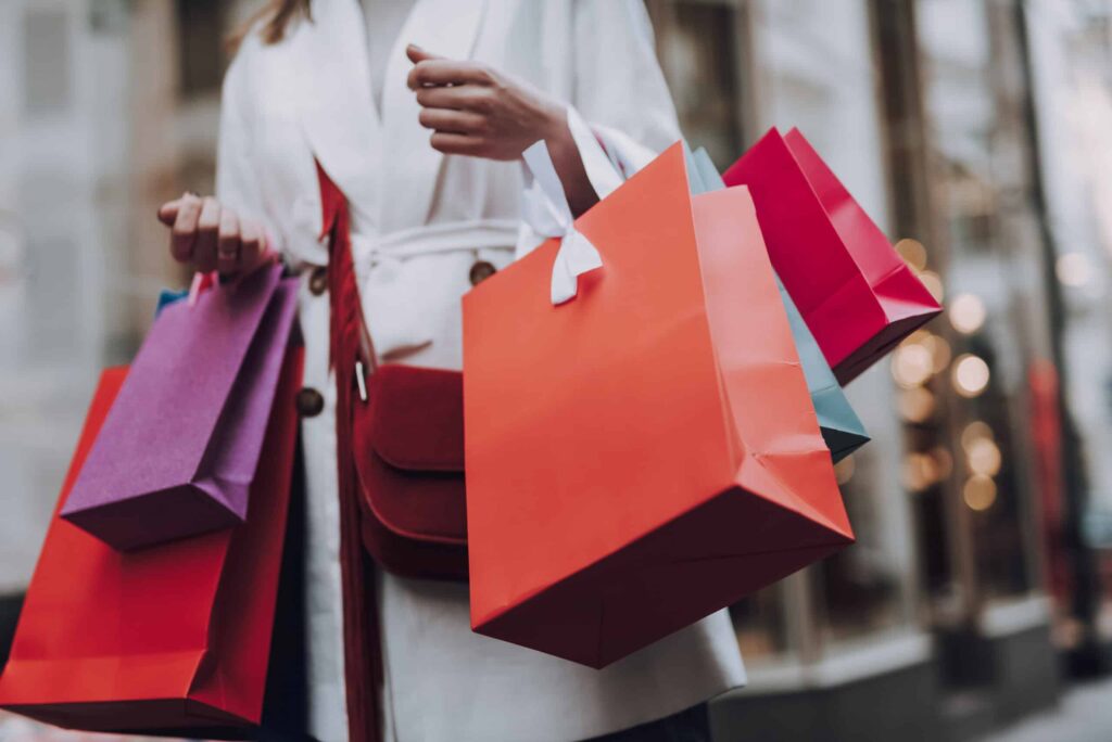 Impulse buying. Close up of lady in white trench coat holding colorful shopping bags