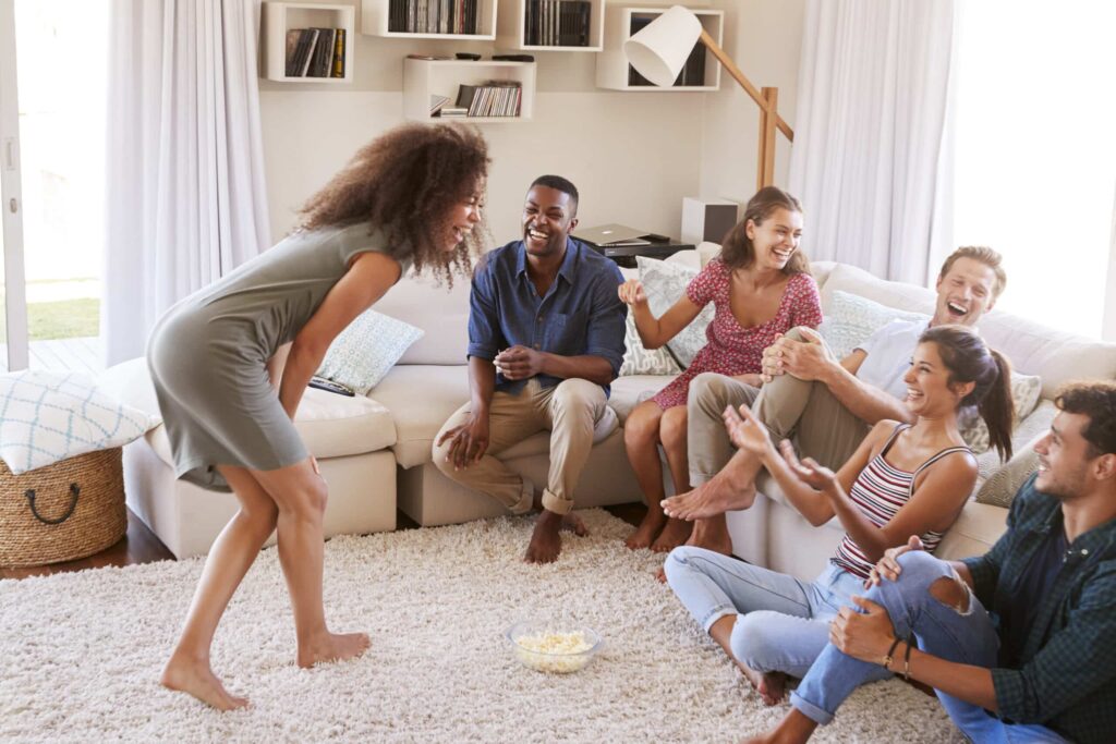 save on entertainment. Group Of Friends At Home Having Fun Playing Charades Together