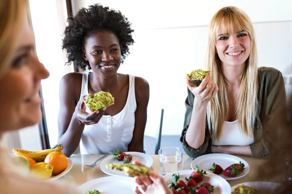 avocado toast. Shot of group of friends laughing while eating healthy food at home.