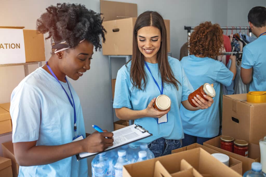 charities. Group of people working in charitable foundation. Happy volunteer looking at donation box on a sunny day. Happy volunteer separating donations stuffs. Volunteers sort donations during food drive