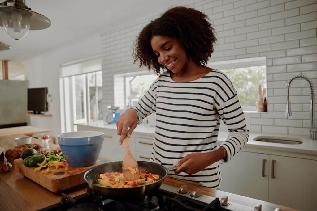 eating well on a budget. Woman mixing ingredients and vegetables in pan while preparing lunch indoors