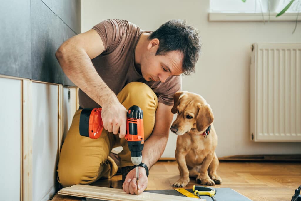 save money. Man doing renovation work at home together with his small yellow dog.