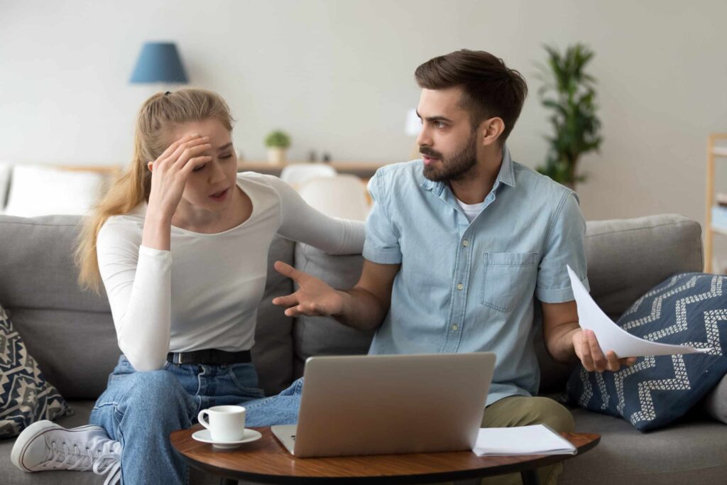 talk about money. Stressed unhappy couple arguing about huge expenses with laptop and papers, angry husband blaming wife of overspending debt, family having conflict fight about wasting money financial problem at home.