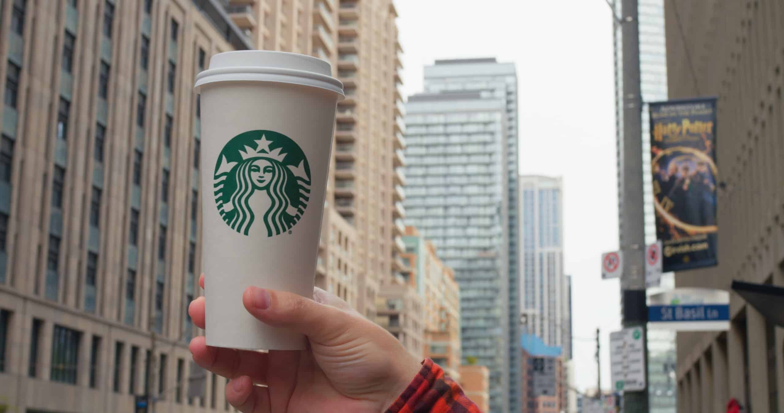 Starbucks drinks. Hand holds Starbucks cup, iconic urban backdrop. City hustle flows as Starbucks offers familiar comfort. Emblematic coffee moment in metropolitan life. Starbucks concept