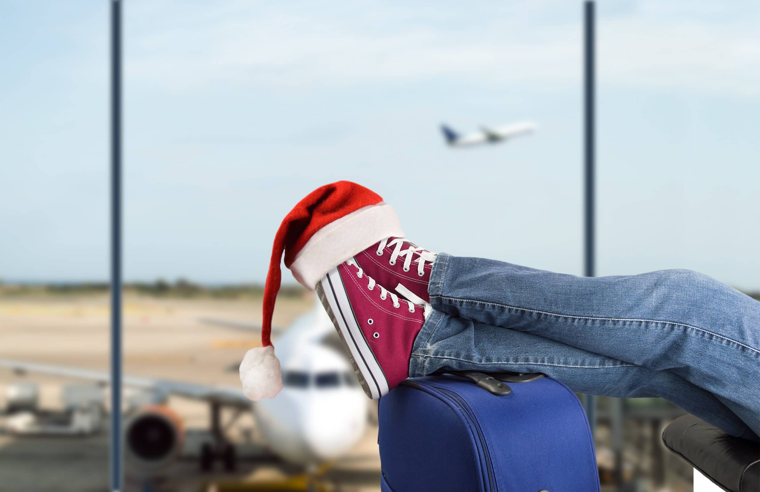 holiday travel. young boy with his legs over the suitcase waiting at the airport with santa hat on the feet