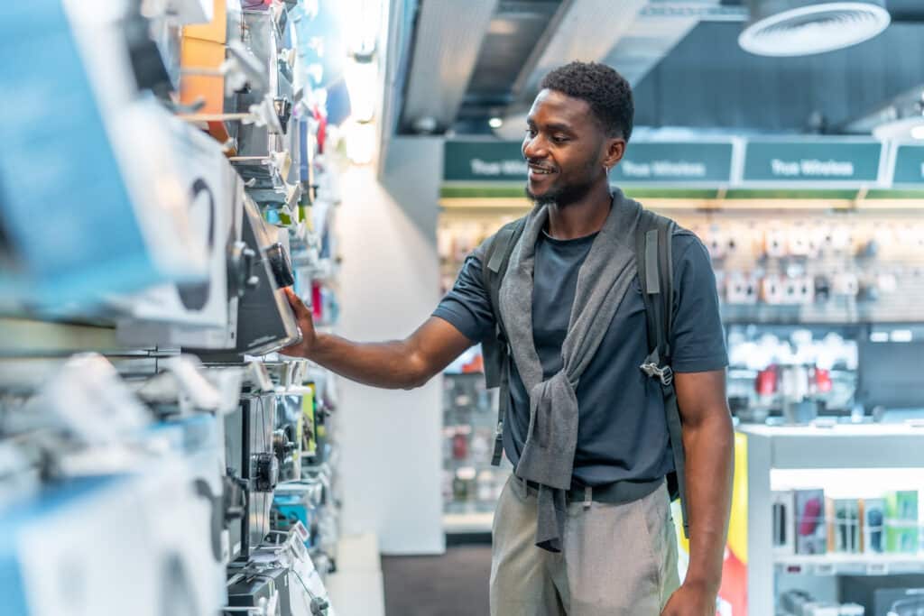 want or need. Side view three quarter length photo of a cheerful african man checking headphones in electronics store